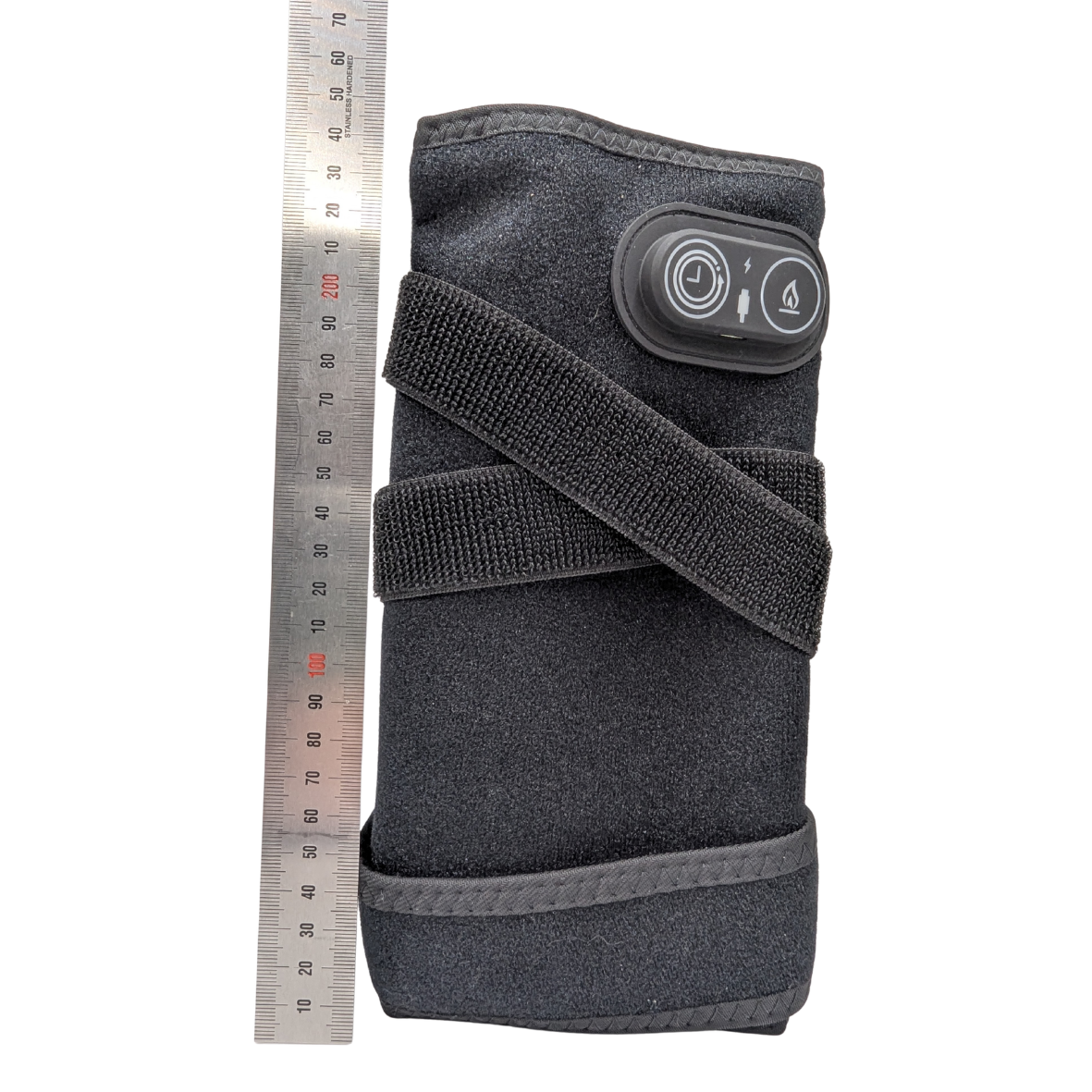 A dark gray fabric wrist wrap or arm sleeve with an adjustable hook-and-loop strap and a black control panel featuring two buttons, shown next to a metal ruler for scale on a white background.