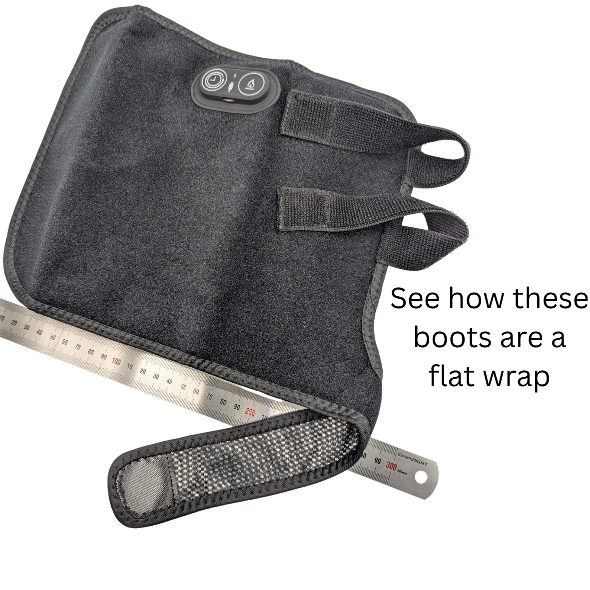 A dark gray heated boot wrap with an integrated control panel and straps, shown alongside metal rulers to demonstrate its flat wrap size, with text reading 'See how these boots are a flat wrap'.