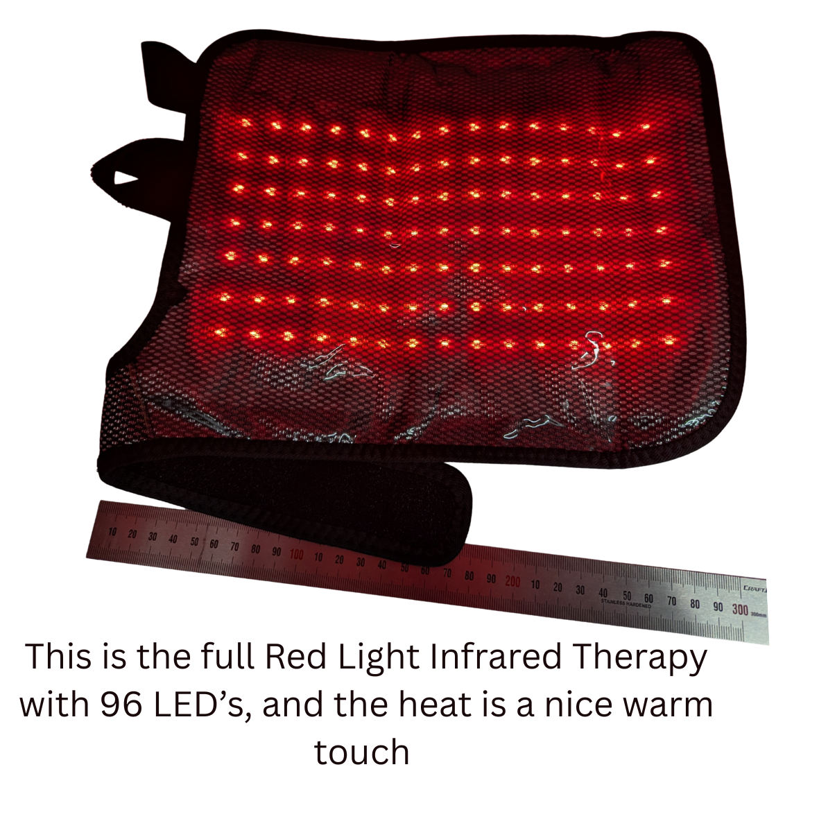 Red light therapy panel with a black mesh cover and wrist strap, shown with a ruler for scale and descriptive text below on a white background.